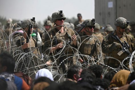 U.S. soldiers guarding behind barb wired fence as Afghans sit near the airport in Kabul, Afghanistan. Afghans hoping to flee the country after the Taliban takes over Afghanistan.